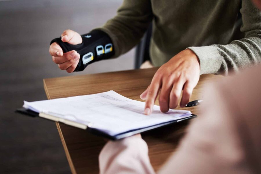 Injury, compensation and man hands with insurance documents, legal contract and paperwork. Disability, accident and people in lawyer or attorney meeting for advice, agreement or policy report closeup Loi Fédérale sur l'Assurance-Accidents (LAA) en Suisse